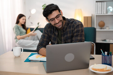 Focused handsome freelancer doing online research over laptop while working at desk in living room. Man with laptop working remotely from home