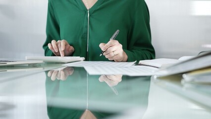 Businesswoman accountant at a sleek glass desk in a contemporary office, using a calculator to crunch numbers and jotting down meticulous notes, green color style. Taxes, audit in business