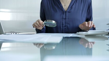 Businesswoman analyzing financial data with magnifying glass and calculator, performing accounting...