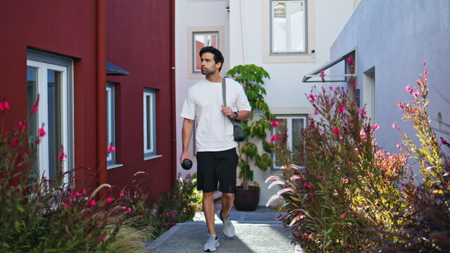 Sporty man walking outdoors with fitness gear surrounded by flowers and greenery