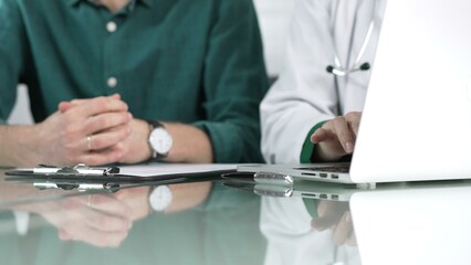 Doctor woman is typing on laptop computer while listening to patient complaints during medical consultation in clinic office. Medicine concept