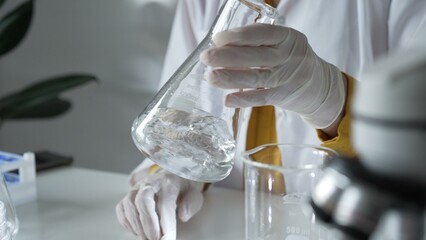 Unknown scientist wearing white protective gloves is carefully shaking up a clear chemical solution...