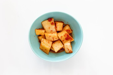 A small bowl of traditional Korean radish kimchi set against a white background.