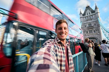 Fototapete Rund Young man taking a selfie in london with a red double-decker bus passing by and tower bridge in the background, enjoying his trip in the capital of england © CarlosBarquero