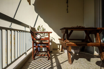 rustic wooden furniture on a sunlit balcony, a white domestic cat laying on a wooden chair, basking in the warm afternoon light. Pets at home behavior.