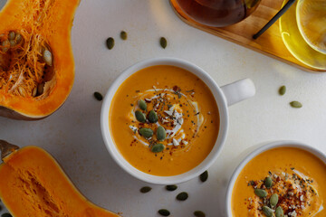 Roasted butternut squash soup with cream and pumpkin seeds on two white mugs.