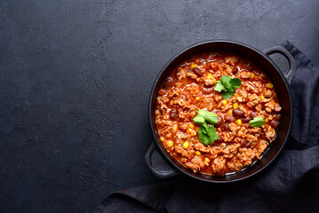 Chili con carne - traditional mexican minced meat and vegetables stew in tomato sauce in a cast iron pan. Top view with copy space.