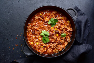 Chili con carne - traditional mexican minced meat and vegetables stew in tomato sauce in a cast iron pan. Top view with copy space.