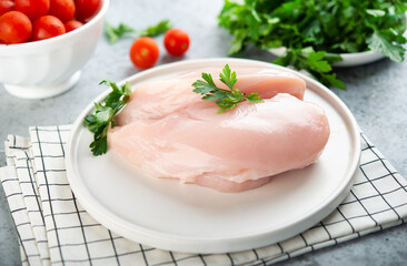 Raw chicken breast for cooking is on a plate with herbs and vegetables