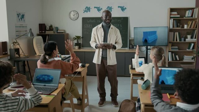 Handheld zoom out shot of active students and African American male teacher during 3D modelling class in modern elementary school