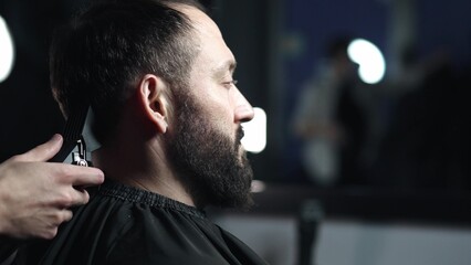 Professional barber wielding electric hair clipper, meticulously grooming bearded client's hair in...