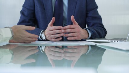 Business partners or lawyers dressed in blue are reviewing and discussing contract papers during a meeting, using a laptop and documents on a glass table. Businesspeople