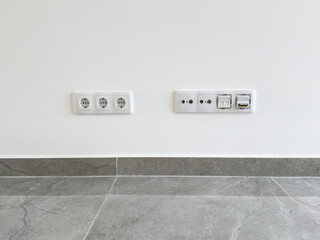 Modern wall with multiple electrical outlets and network ports above a tiled floor.