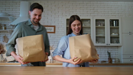 Shopping couple entering kitchen unpacking groceries in white interior closeup