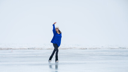 Caucasian woman in a blue sweater is skating on a frozen lake. The figure skater performs the...