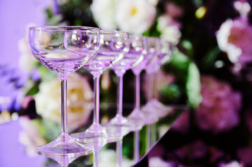 Row of empty champagne coupe glasses arranged in a line on a reflective surface, creating a visually appealing effect