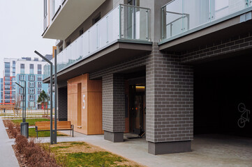Modern apartment building with a contemporary design featuring a combination of glass, wood, and dark brick. Wooden panel indicates the entrance