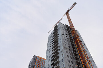 High-rise building under construction with large construction crane. Visible balconies and windows...