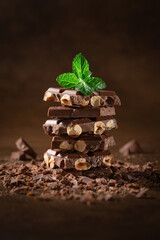 Dark and milk chocolate with nuts on a dark background sprinkled with cocoa powder. Chocolate pieces with almonds and hazelnuts close-up.