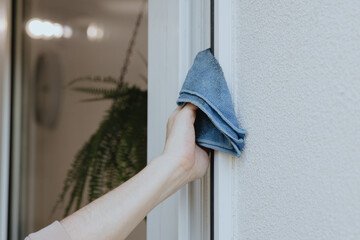 One young man washes a window frame with a blue rag.