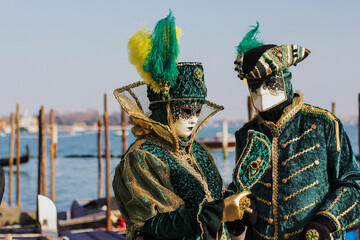 Pair of beautiful Venetian masks on the Grand Canal background, traditional festival in Venice, close-up, faces, two green and gold carnival costumes, masquerade, Venice, Italy.