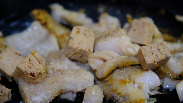 Cooking Indoors pan grilled seasoned Cod fillets and Tofu with spices and sun-dried tomatoes. On Stovetop, iron cast skillet, close up boiled oil, process deep fried.