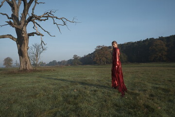 Young beautiful slender woman in a fashionable red dress. Woman posing in the fog morning sunrise...