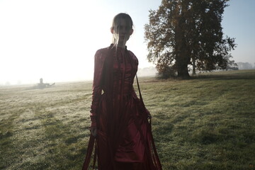 Young beautiful slender woman in a fashionable red dress. Woman posing in the fog morning sunrise...