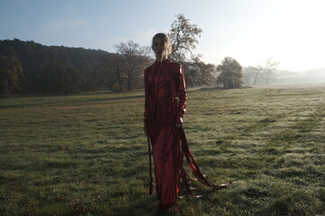 Young beautiful slender woman in a fashionable red dress. Woman posing in the fog morning sunrise nature. Advertising of fashionable womens clothing