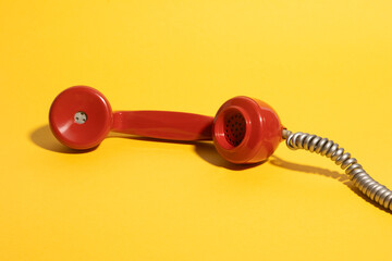 A retro red telephone handset with a coiled cord lying on a vibrant yellow background, creating a...