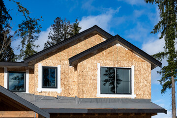 New home construction, house exterior with wood OSB, oriented strand board, walls up and windows installed and roof base layer and moisture barrier on, sunny winter day on the job site
