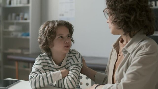 Caring mother talking to little son at desk in medical office, supporting and comforting child during health check-up