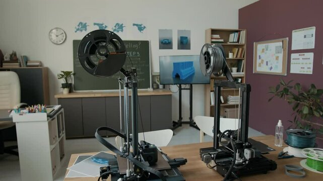 No people handheld zoom out shot of interior of modern school 3D modelling classroom with two 3D printers, large TV screen and chalkboard
