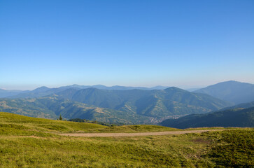 Serene view of rolling mountains under bright blue sky, showcasing lush greenery and distant peaks, perfect for highlighting tranquility, nature's beauty, and peaceful landscapes. Carpathians, Ukraine