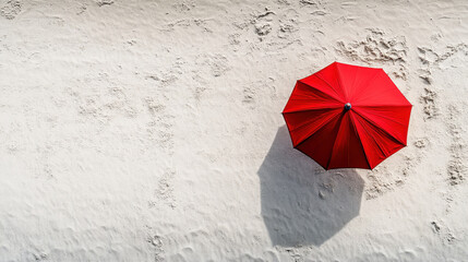 A striking red umbrella captured from a bird's-eye view on a textured white sand beach