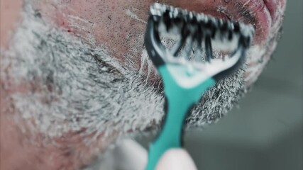 Close up of a man shaving his beard with a razor