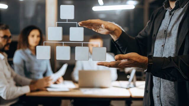 A closeup of a facilitators hands gesturing towards a floating 3D model of a digital workflow surrounded by focused team members strategizing their corporate transformation.