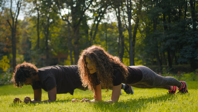 Indian Arabian man and Caucasian woman fitness couple planking on yoga mat together in city park sporty male female friends athletes strength training sport exercise healthy lifestyle workout outdoors