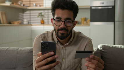 Happy Arabian Indian man customer bank client credit card holder with mobile phone pay in banking...