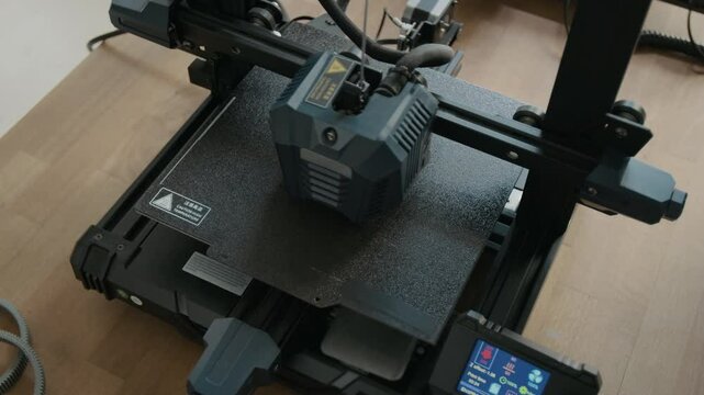 Top view close-up shot of 3D printer with textured build platform actively printing object on wooden table