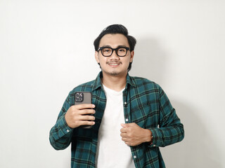 Smiling satisfied young Asian man wearing a white checkered shirt holding a mobile phone isolated on white background