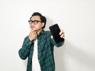 Portrait of a thinking handsome young Asian man wearing a plaid checkered shirt showing mobile phone with a blank screen isolated o on white background