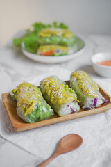vegetables wrapped in rice paper, placed on a plate in a row of 3 pieces. the contents are chicken, lettuce, purple cabbage, instant noodles