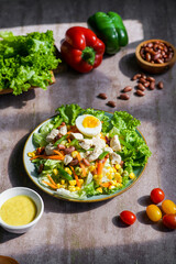 a vegetable salad on a plate containing lettuce, egg slices, purple cabbage, carrots, chicken, corn