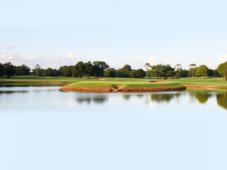 Obraz premium Beautiful Golf Course Landscape Featuring Lush Green Fairways and Tranquil Pond Under Clear Blue Sky