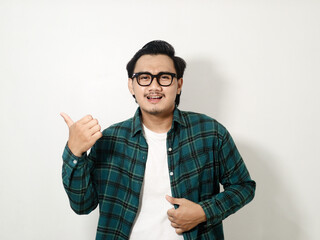 Smiling young handsome Asian man wearing a plaid shirt pointing finger at empty copy space isolated on white background