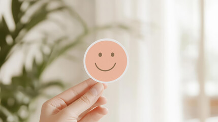 Hand holding smiley face sticker in bright room, conveying happiness
