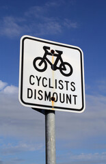 Cyclists Dismount road sign mounted on a metal pole against a blue sky with clouds background