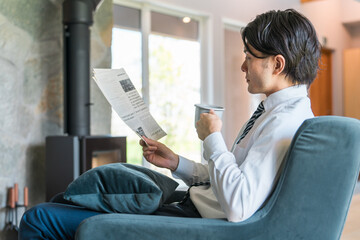 朝家で英字新聞を読むスーツ姿のアジア人ビジネスマン
