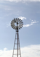 Windmill backlit against a blue sky with scattered clouds